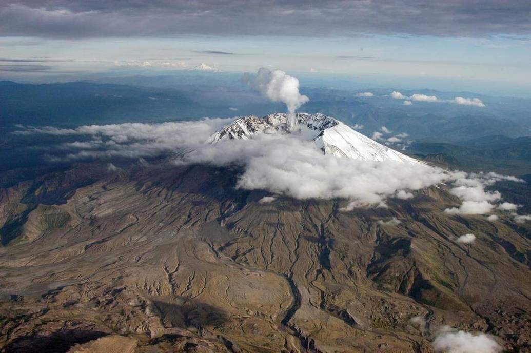 A steep snow-capped stratovolcano above cloud.